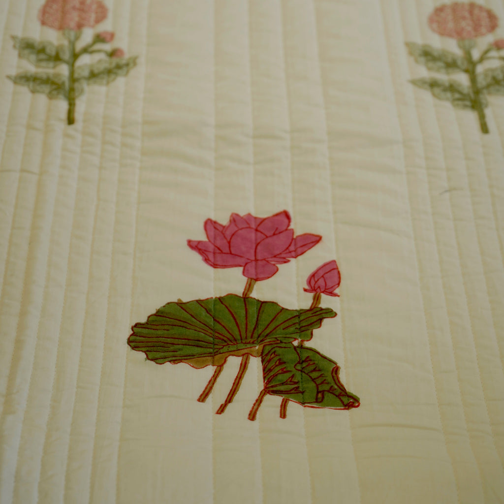 A close-up of a quilted cream-colored fabric featuring embroidered pink lotus flowers and green leaves.