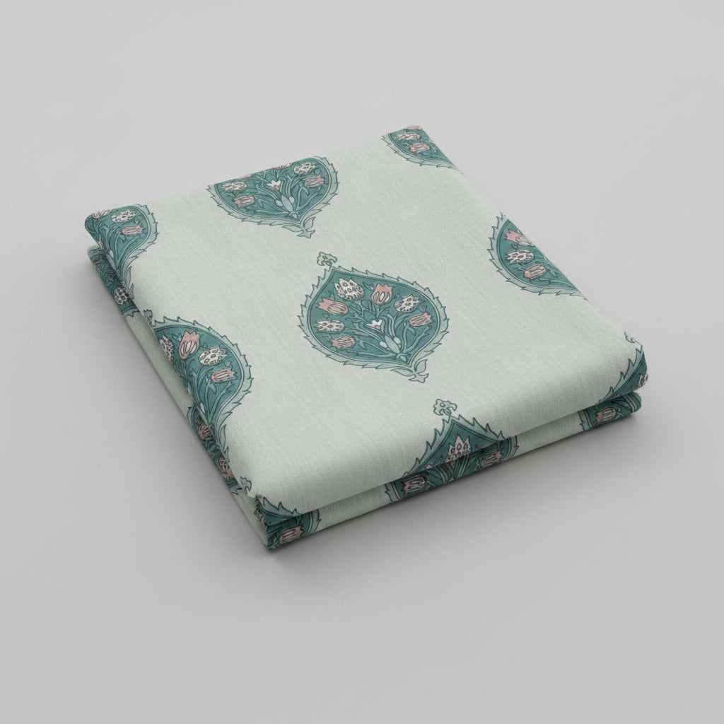 A bed made with a white cotton block-print bedding set featuring teal and pink floral motifs, with two matching pillowcases and a decorative book placed on top.